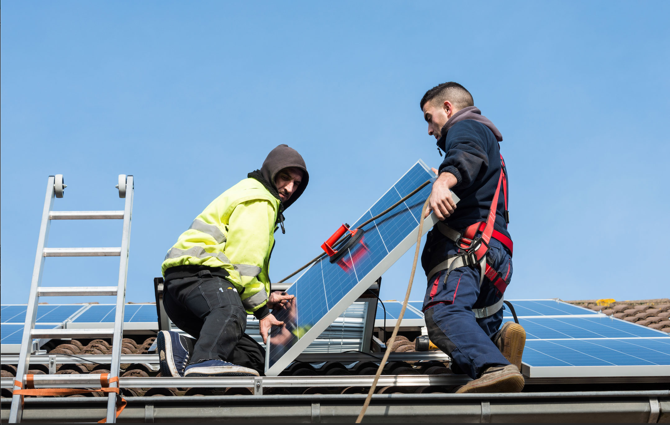 Two installers putting solar panels on a pitched roof.